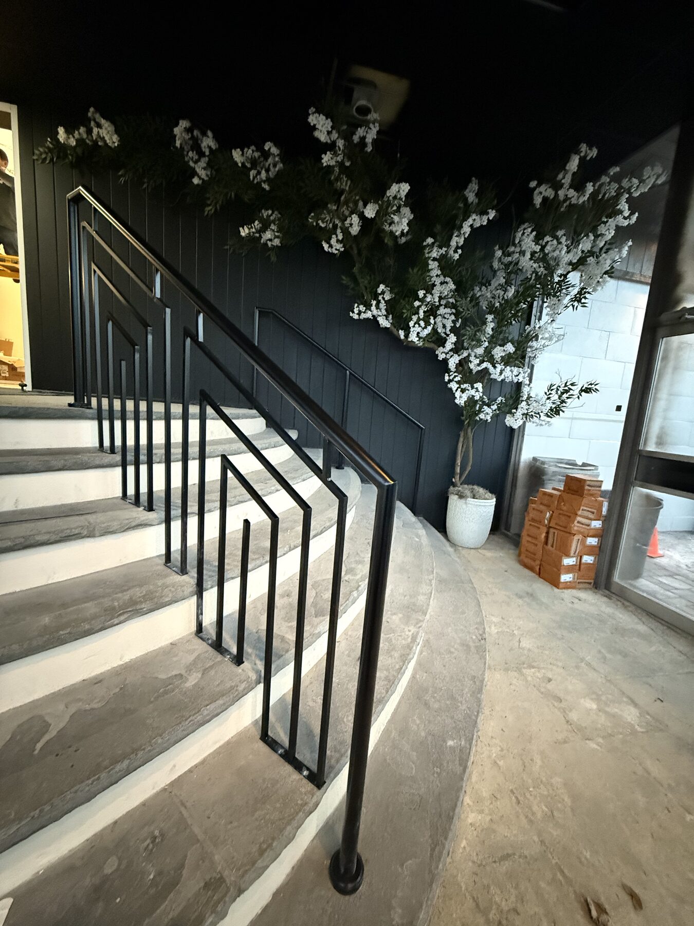Black metal railing following a curved set of stone steps, with vertical pickets and rectangular decorative details